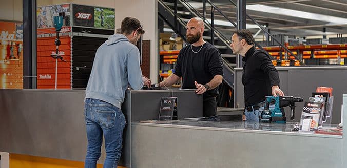 Twee medewerkers van AIC Visser helpen een klant aan een balie met gereedschap op de toonbank.